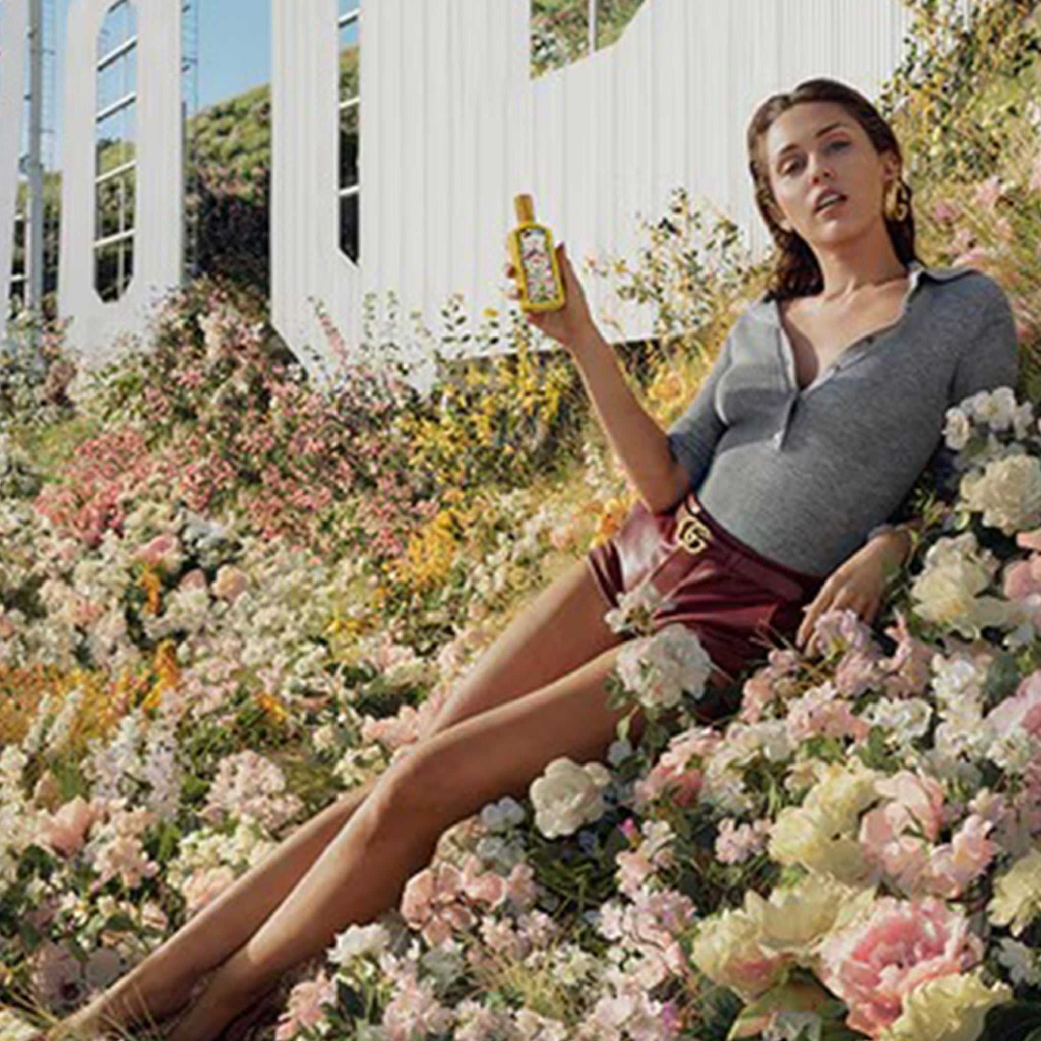 Woman holding Gucci Flora Gorgeous Orchid Eau de Parfum 100ml in a floral field, showcasing its feminine and exotic appeal.