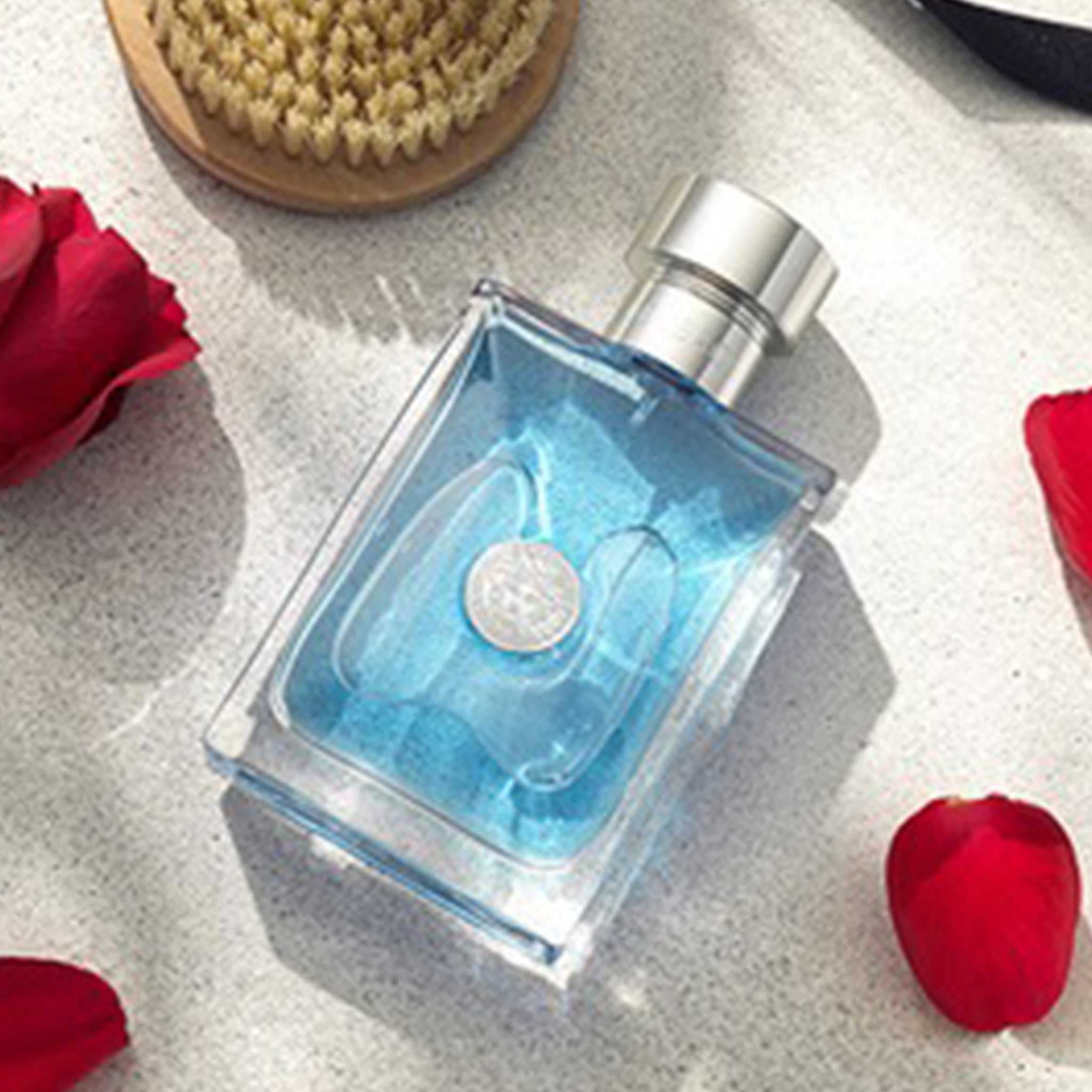 Versace Pour Homme Eau de Toilette 100ml bottle lying on a light surface with rose petals and grooming brush, highlighting its fresh masculine appeal.